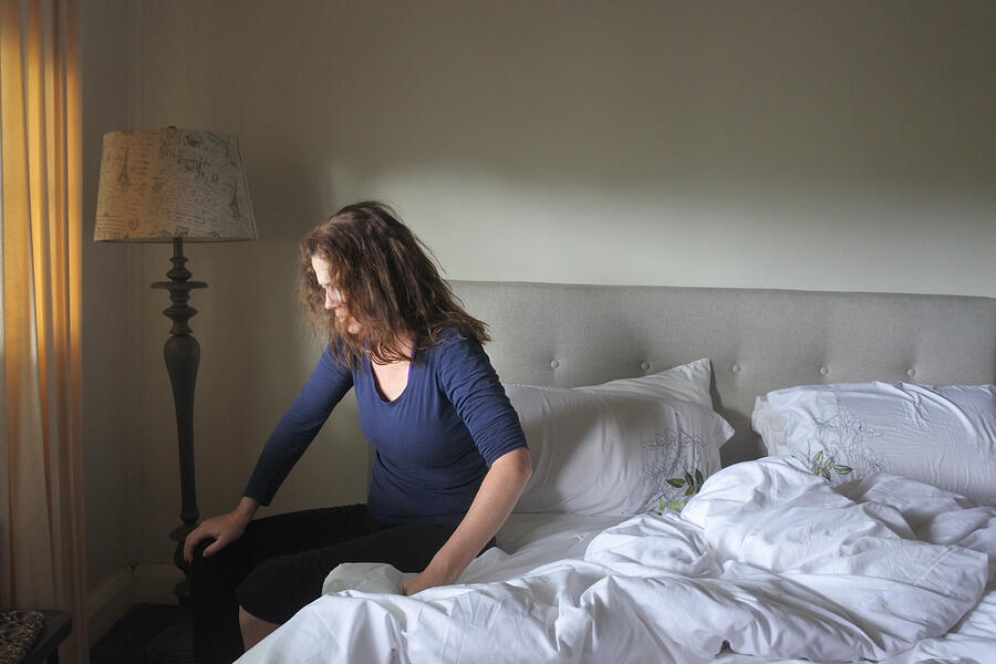 Sad adult woman sitting on bed confused and exhausted Photograph by Rafael Ben-Ari