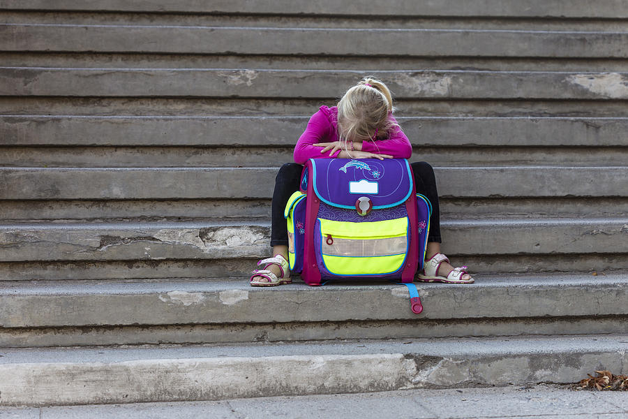 Sad little girl sitting on stairs with school bag Photograph by Westend61
