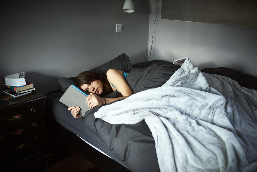 Sad looking woman lying in bed with tablet reading messages Photograph by 10000 Hours