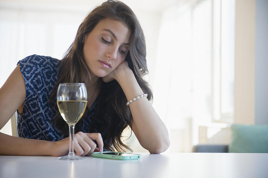 Sad woman with glass of wine texting Photograph by Jamie Grill