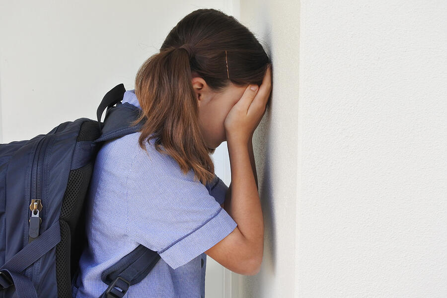Sad young schoolgirl covering her face and crying against a wall Photograph by Chameleonseye