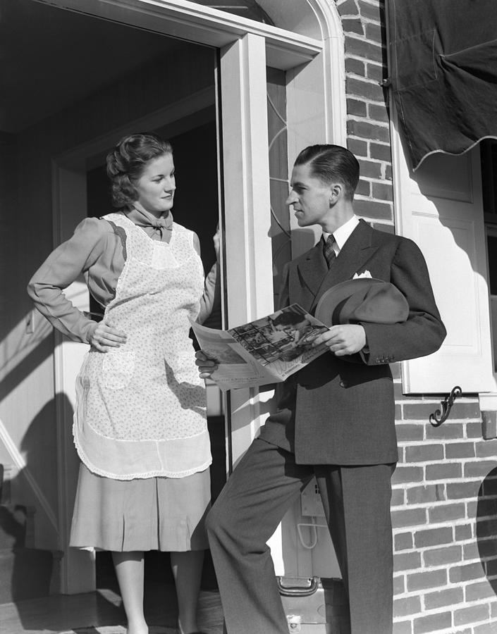 Salesman At Door Of A House Wife Showing Her A Brochure Of His Product He Is Dressed Ia A Suit She Is Wearing A White Apron Over A Dressey Dress. Photograph by H. Armstrong Roberts