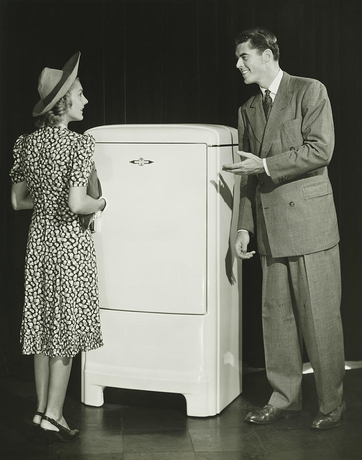Salesman presenting refrigerator to woman in studio, (B&W) Photograph by George Marks