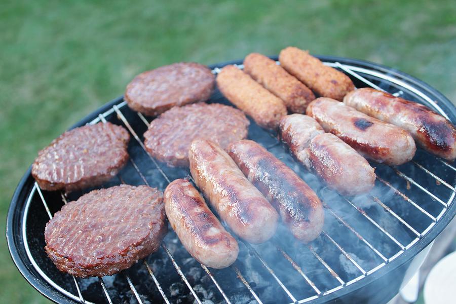 Sausages and burgers cooking on barbecue Photograph by Neil Langan Uk
