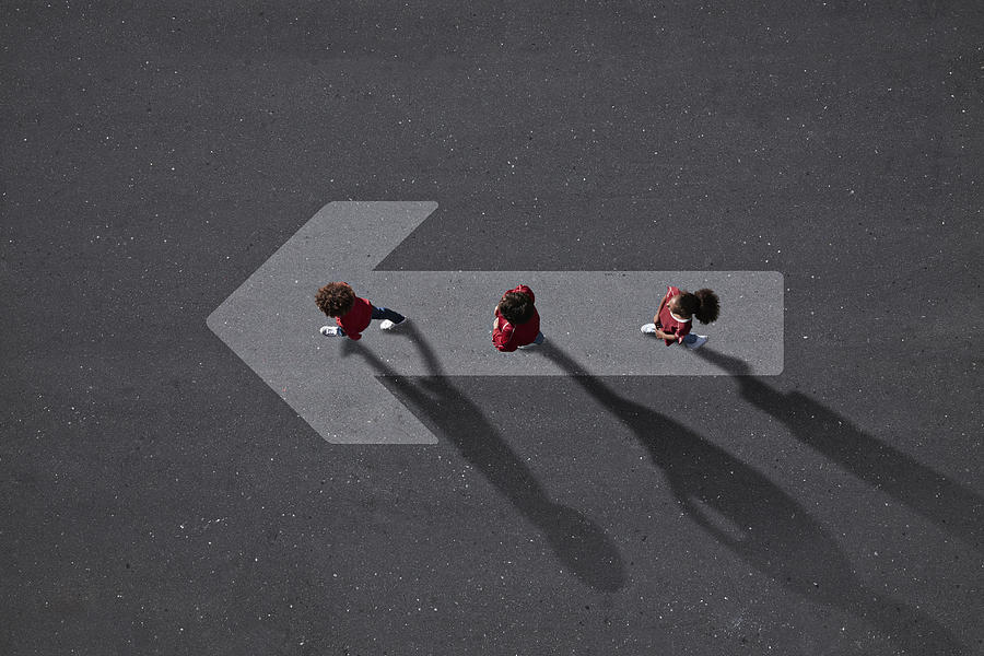 School children dressed in red, walking across big painted arrow Photograph by Klaus Vedfelt