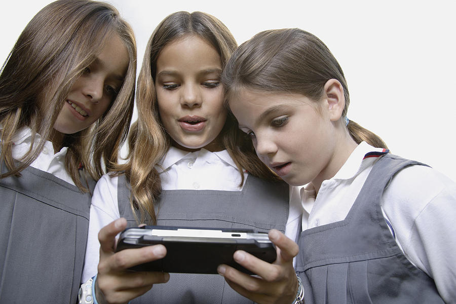 School girls playing handheld video game Photograph by Floresco Productions