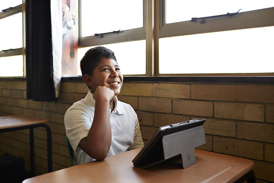 Schoolboy in class laughing with tablet in front Photograph by Klaus Vedfelt