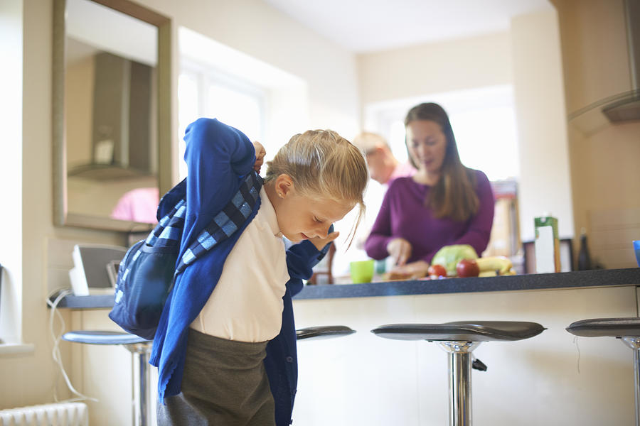 Schoolgirl putting on school satchel in kitchen Photograph by Peter Muller
