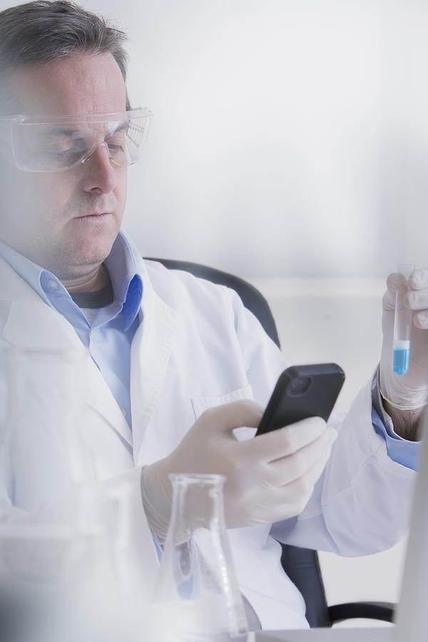 Scientist holding smartphone and test tube Photograph by REB Images