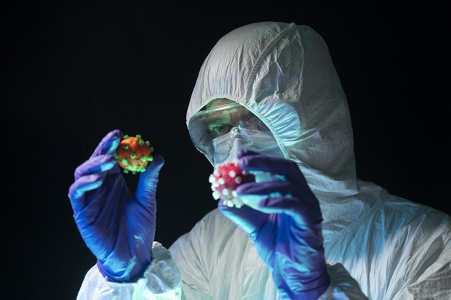 Scientist in a protective suit holds and compares two different Coronavirus of different color in his hands. Creative image. Photograph by Aitor Diago