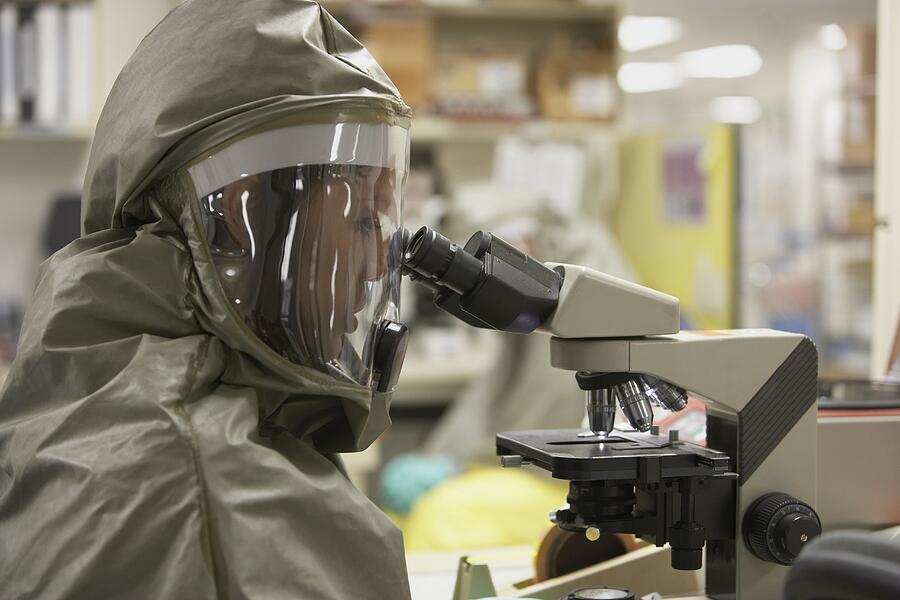 Scientist in hazmat suit looking into microscope Photograph by ER Productions Limited