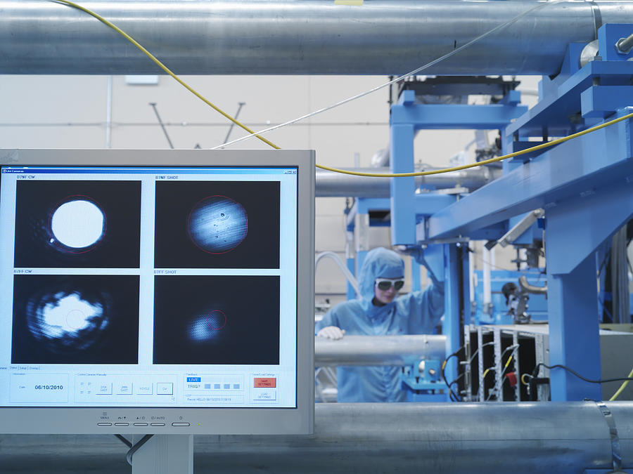 Scientist wearing protective clothing and goggles in laser laboratory performing an experiment shown on the monitor in the foreground Photograph by Monty Rakusen