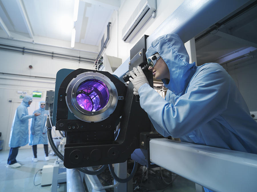 Scientists in protective clothing and goggles in laboratory next to laser equipment Photograph by Monty Rakusen