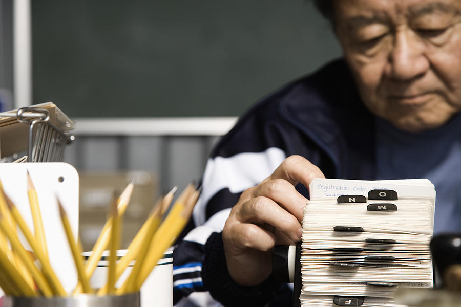 Senior Asian man looking at circular card file Photograph by Hill Street Studios