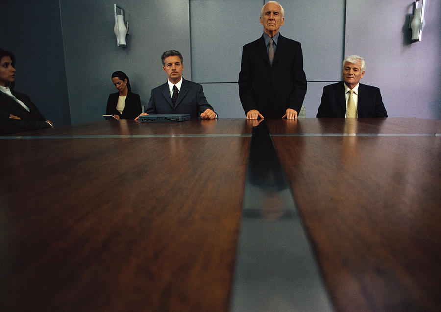 Senior businessman standing at conference table while others are seated, long shot Photograph by Laurence Mouton