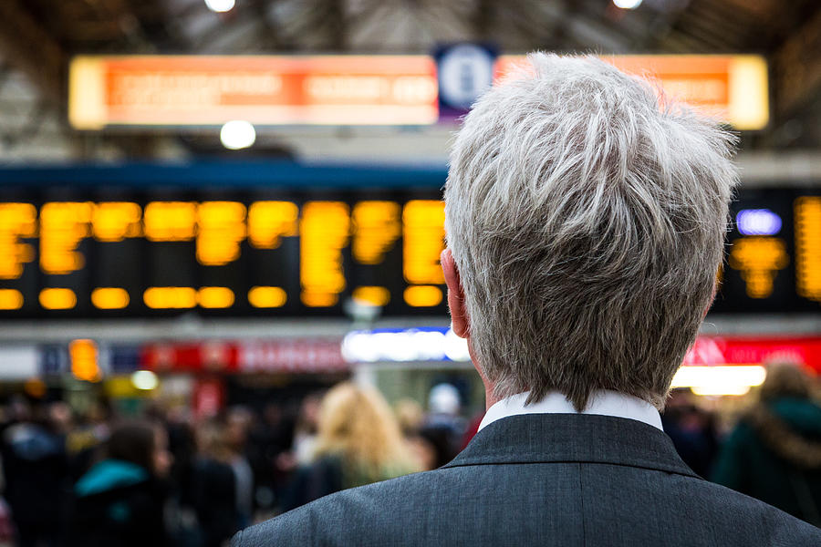 Senior businessman waiting for train with departure boards in background, London, UK Photograph by Coldsnowstorm