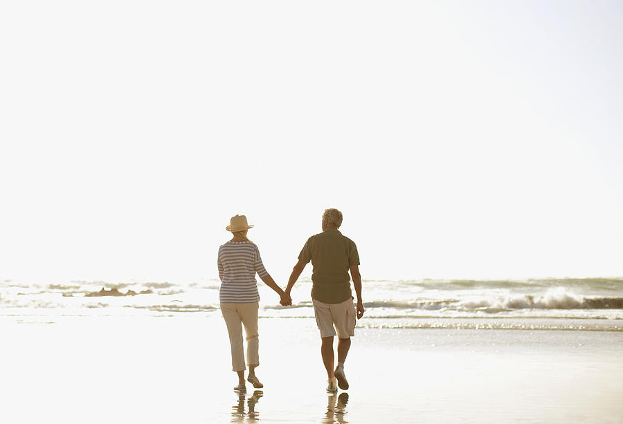Senior couple holding hands and walking on beach Photograph by Tom Merton