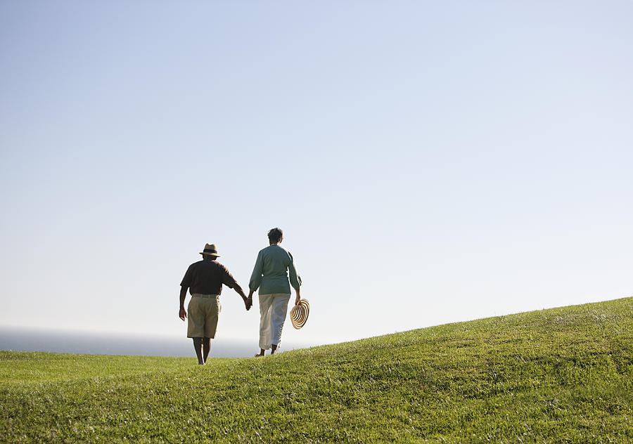 Senior couple holding hands on grassy hill Photograph by Robert Nicholas