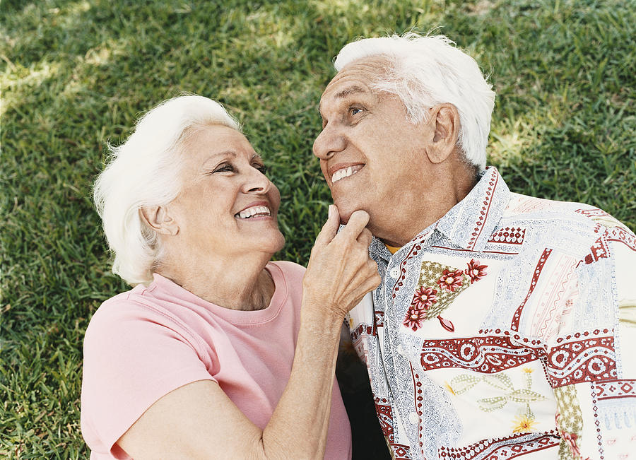 Senior Couple Lie on the Grass, Embracing Photograph by Digital Vision.
