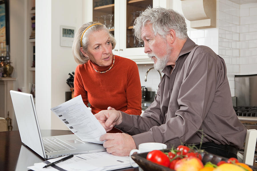 Senior couple looking concerned with bills and laptop Photograph by Image Source