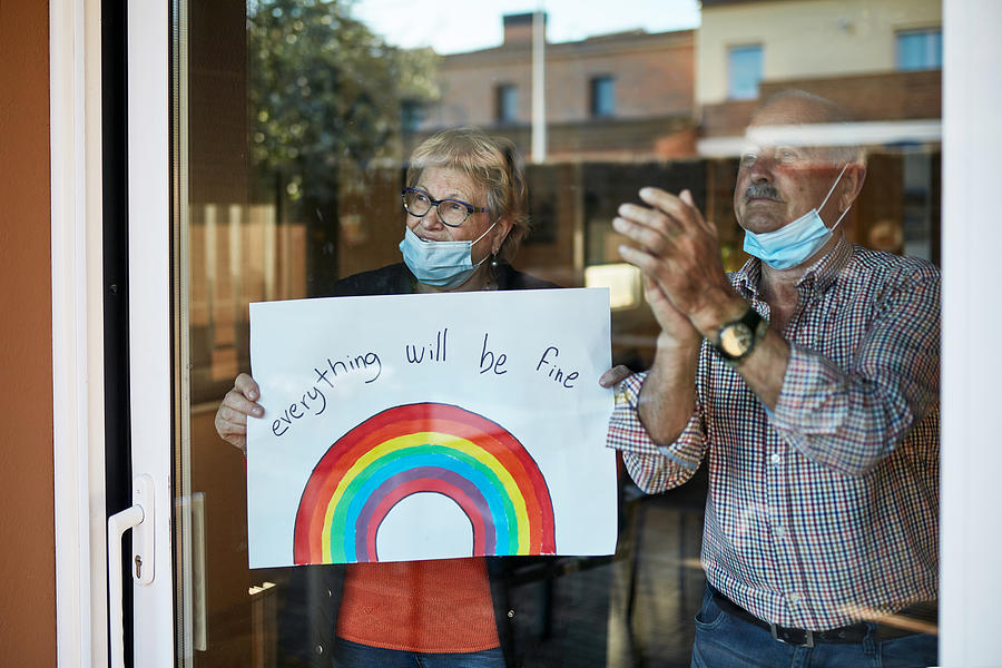 Senior couple on their 70s clapping hands at showing a hand drawn rainbow at home in quarantine Photograph by Xavierarnau