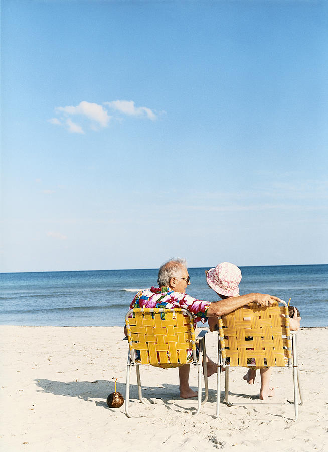 Senior Couple Sit on Deckchairs on the Beach, Talking Photograph by Digital Vision.