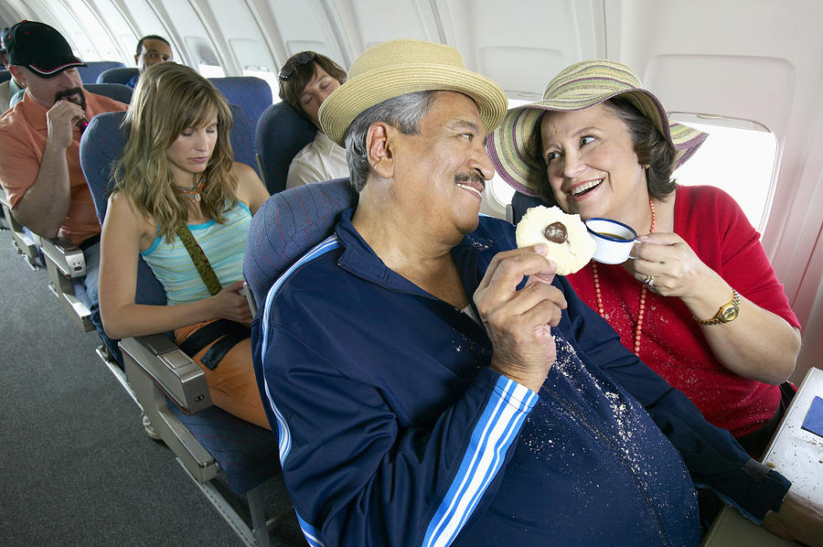 Senior Couple Sitting in an Aircraft Cabin Eating and Drinking Photograph by Digital Vision.