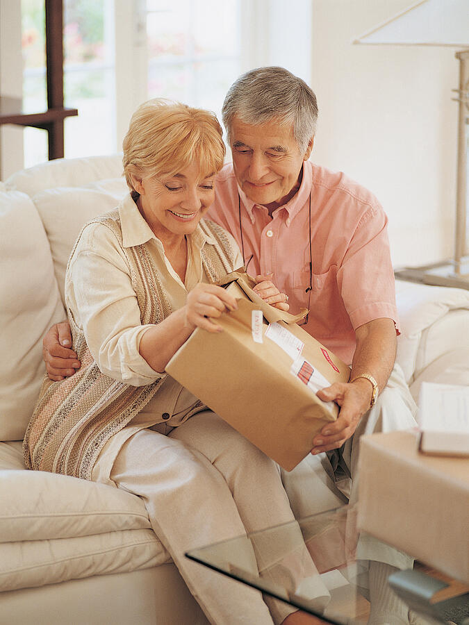 Senior Couple Sitting on a Sofa at Home and Opening a Parcel Photograph by Flying Colours Ltd