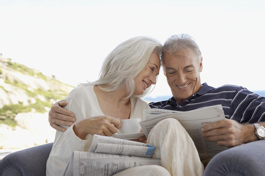 Senior Couple Sitting Together in an Arm Chair and Reading a Newspaper Photograph by Digital Vision.