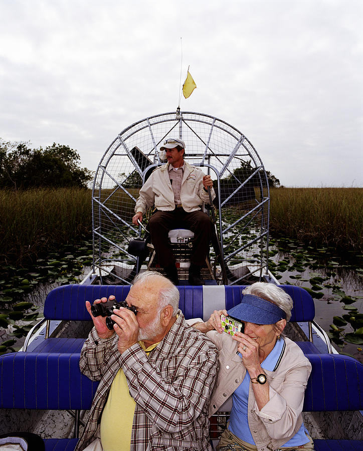 Senior couple taking photos on airboat, driver in background Photograph by Ryan McVay