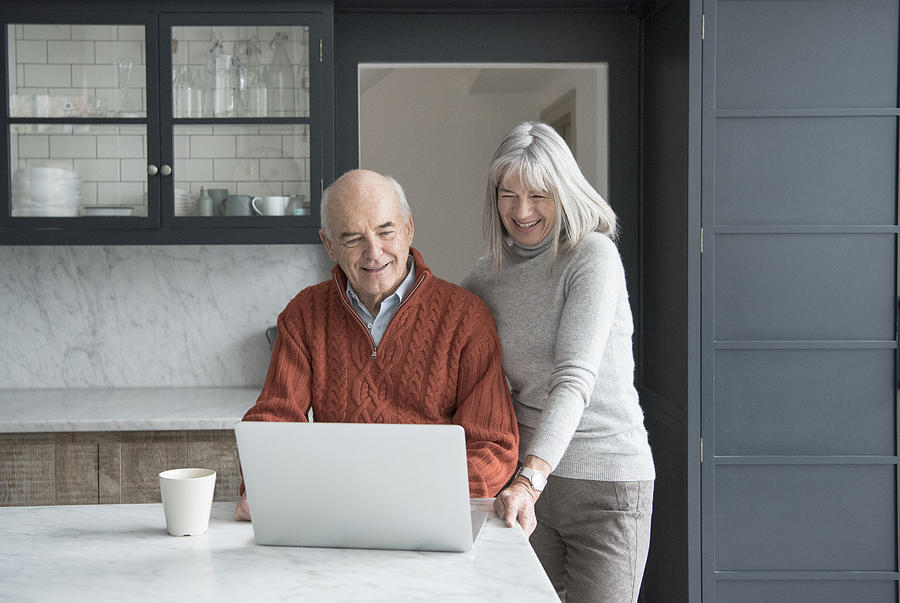 Senior couple using laptop in kitchen Photograph by JohnnyGreig