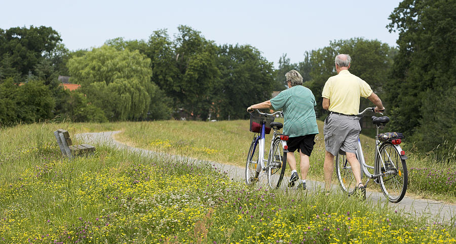 Senior couple walking with bicycles in summer on dyke Photograph by RelaxFoto.de