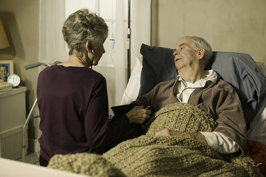 Senior doctor checking blood pressure of senior man in bed in retirement home Photograph by Photodisc
