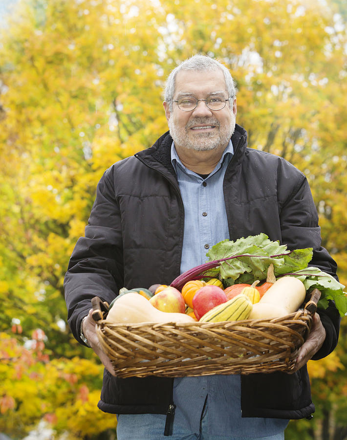 Senior Hispanic man carrying basket of vegetables Photograph by John D. Buffington