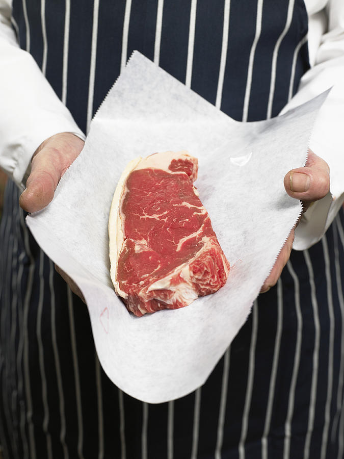 Senior male butcher holding sirloin of steak, mid section Photograph by Michael Blann