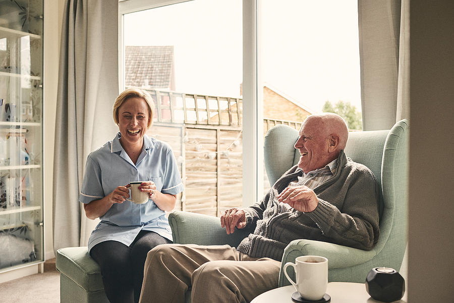 Senior man and female carer enjoying coffee at home Photograph by Dean Mitchell