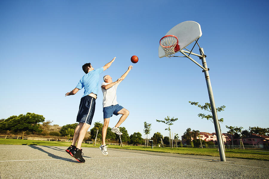 Senior man and young man playing basketball on outdoor court Photograph by Peter Griffith