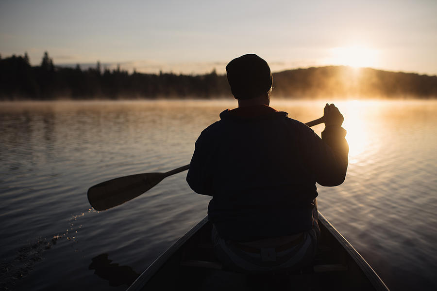 Senior man canoeing on lake at sunset, rear view Photograph by Hugh Whitaker
