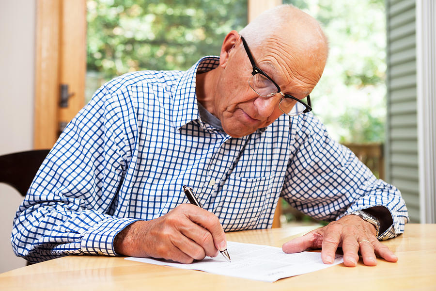 Senior Man Filling Out Paperwork, Signing Document Photograph by BanksPhotos