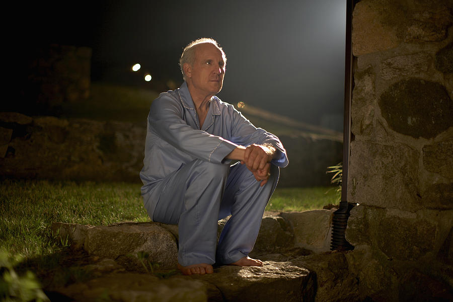 Senior man in pyjamas sitting outside house at night Photograph by Kim Carson