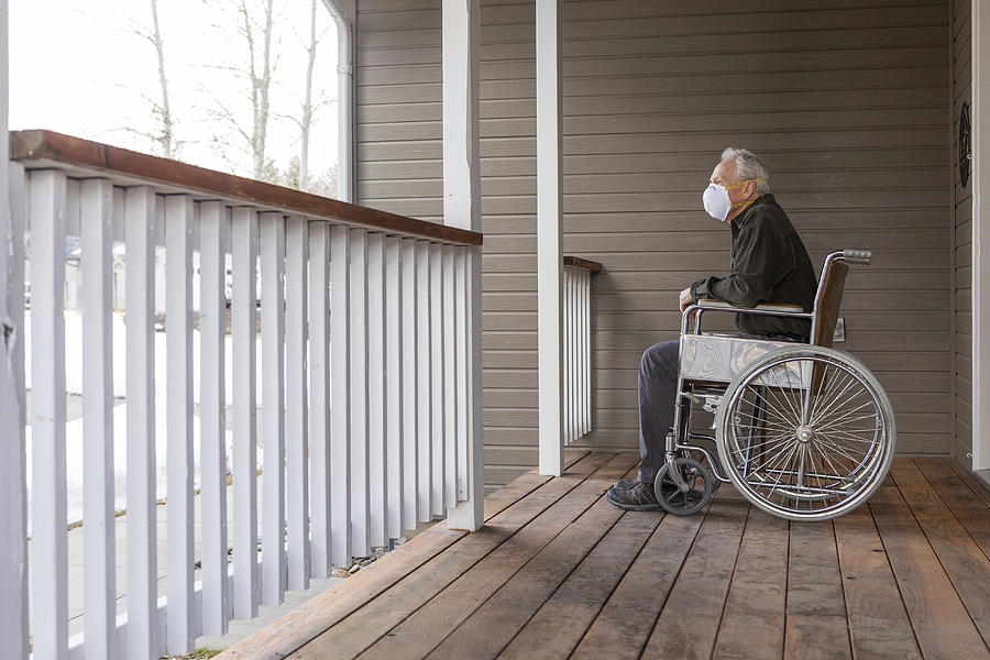 Senior man in wheelchair wearing protective mask to prevent coronavirus transmission on porch Photograph by Steve Smith