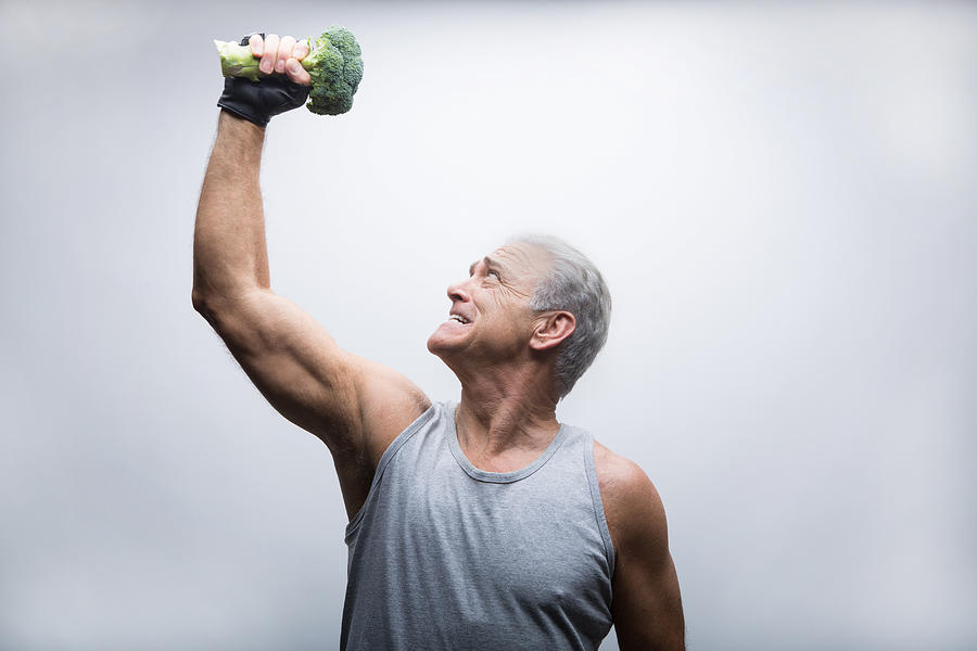 Senior man looking up and lifting broccoli Photograph by David Jakle