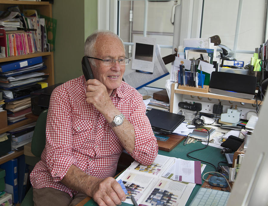 Senior man on phone in home office Photograph by Jenny Cundy