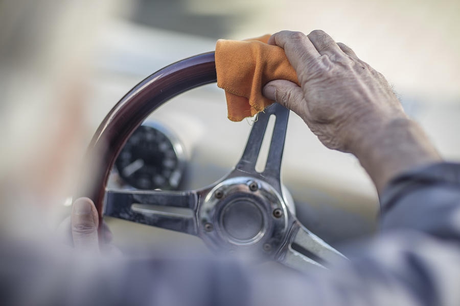 Senior man polishing steering wheel of a car Photograph by Westend61