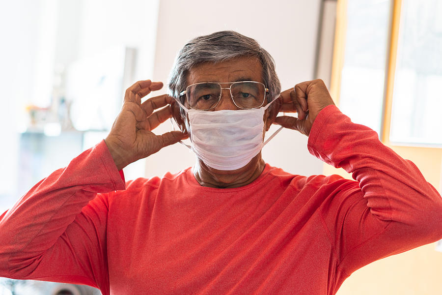 Senior man putting a protective mask on her face Photograph by MesquitaFMS