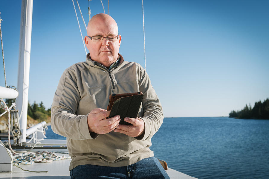 Senior Man Reading On Digital Tablet On His Sailboat Photograph by Mlenny