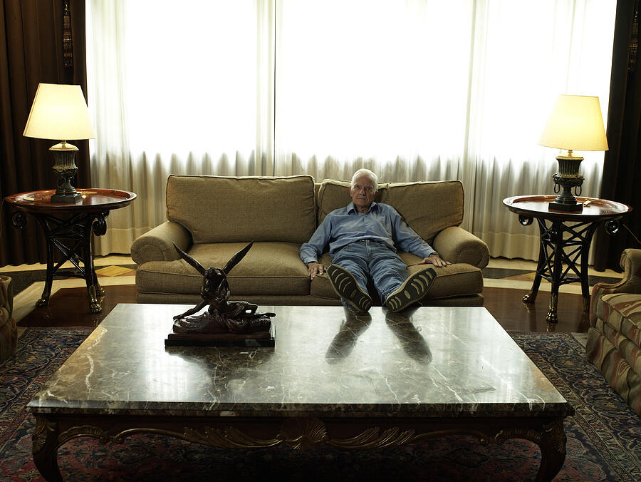 Senior man relaxing on sofa, propping feet on table Photograph by Hans Neleman