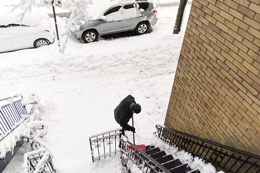 Senior man shoveling snow from stair case on city street. Photograph by Martinedoucet