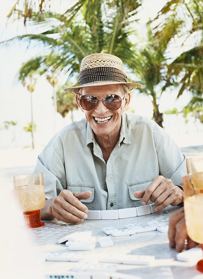 Senior Man Sits at an Outdoor Table Playing Dominoes, Laughing Photograph by Digital Vision.