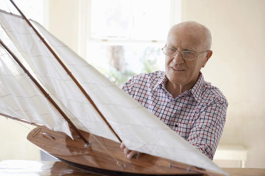 Senior Man Sitting at a Table and Examining a Model Yacht Photograph by Digital Vision.